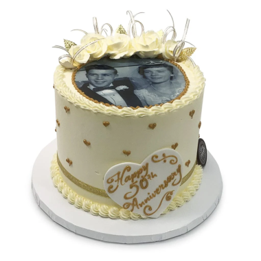 Single-tier cream-colored edible image cake featuring a black and white couple's portrait photo centered on top. This elegant photo cake from Mia's Bakery is decorated with gold heart confetti design around the sides, yellow roses, and "Happy Anniversary" text in gold script. The personalized edible photo print creates a romantic centerpiece perfect for wedding anniversaries and couple celebrations.