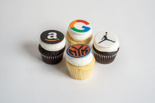 Set of five edible image cupcakes featuring corporate logos including Google, Amazon, Jordan, and Sifra printed on round fondant toppers. These custom photo cupcakes from Mia's Bakery showcase chocolate and vanilla bases with white frosting, topped with high-quality edible printed brand logos. Perfect for corporate events, tech company celebrations, and brand-themed parties using professional edible image printing on cupcakes.