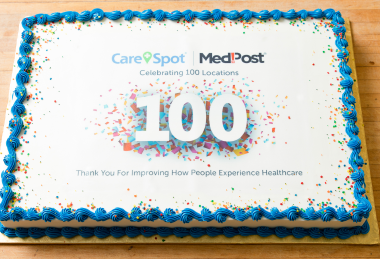 Rectangular white edible image cake featuring company logo and "100 years that matter" text printed on edible sugar sheet. This corporate anniversary photo cake from Mia's Bakery showcases clean minimalist design with blue piped shell borders around the edges. Perfect for corporate centennial celebrations and company milestone events, featuring professional edible image printing on smooth white buttercream frosting.