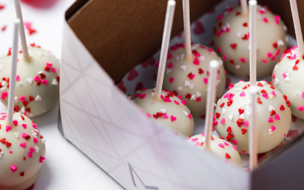 White chocolate cake pops decorated with pink and red heart sprinkles in gift box, perfect valentines dessert ideas for parties and celebrations