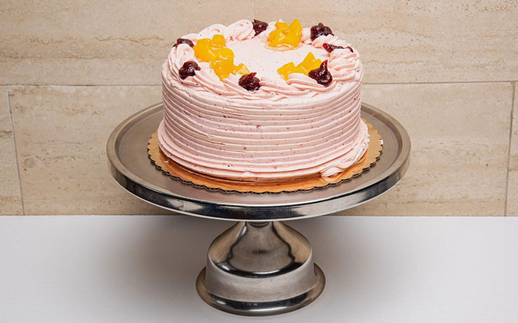 Seasonal desserts for summer featuring berry layer cake with pink buttercream and fresh fruit garnish on cake stand