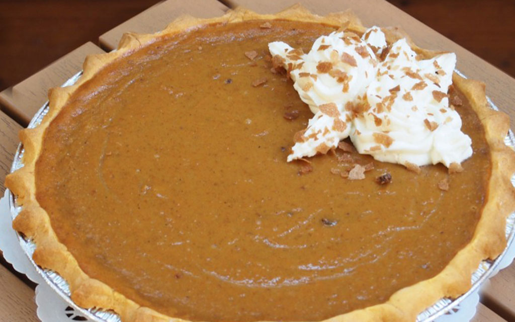 Classic pumpkin pie with whipped cream topping, one of the most popular thanksgiving desserts served on a wooden table