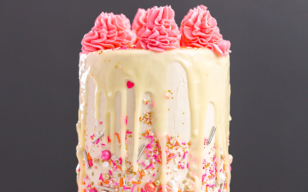 Funfetti wedding cake with colorful sprinkles, white chocolate drip, and pink buttercream rosettes